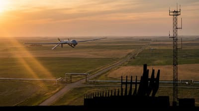Long-endurance commercial drone over rural North Dakota farmland and oil and gas infrastructure at dusk, with ground radar and command-and-control tower in the foreground